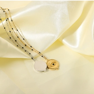 Close-up of evil eye pendant necklaces in gold and silver on yellow silk fabric