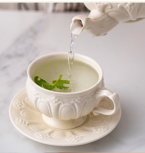 Action shot of tea pouring into a vintage embossed ceramic cup on marble surface