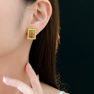 Close-up of vintage gold square stud earring with green enamel and red cross gemstone