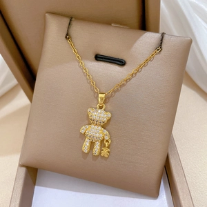 Close-up of a gold teddy bear necklace with clear crystals in a beige jewelry box