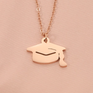 Macro view of rose gold graduation cap pendant necklace on soft pink silk fabric