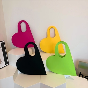 Minimalist heart-shaped felt handbags in rose, yellow, black, and green on white pedestals