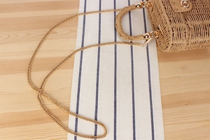 Detail of a golden metal chain strap and woven straw texture with a twist lock
