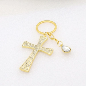 Detail of a golden cross keychain featuring sparkling rhinestones and a teardrop charm