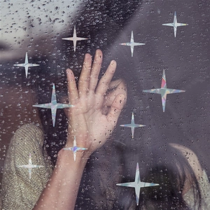 Macro shot of holographic star-shaped window stickers on glass with raindrops and hand detail