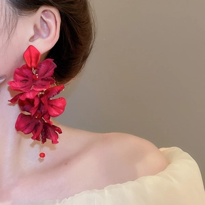 Detailed view of red fabric flower earrings with long tassels on a fashion model