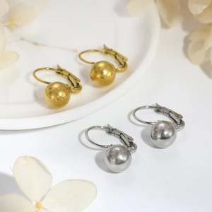 Close-up of gold and silver ball drop earrings on white ceramic with dried flowers