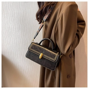 Close-up of black marble leather bag with gold hardware and colorful ethnic strap
