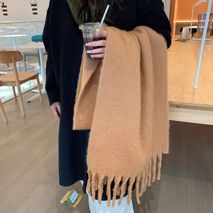 Solid camel mohair knit scarf with fringe detail worn by model in a cozy cafe setting