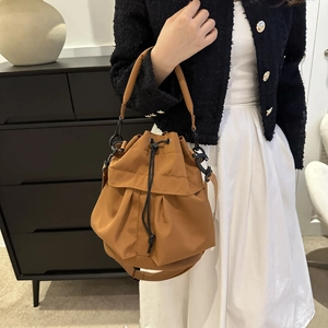 Sac seau en nylon marron avec cordon et deux bandoulières porté par un mannequin chez soi