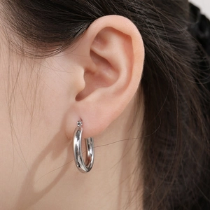 Close-up of polished silver stainless steel hoop earring worn on a person's ear