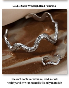 Close-up of polished silver wavy bangle and ring set on textured marble background