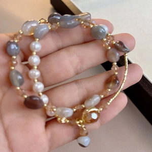 Double-layered beaded bracelet with white pearls and brown agate stones on a person's wrist