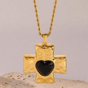 Gold hammer-textured cross necklace with a black heart gem on a vintage stone display