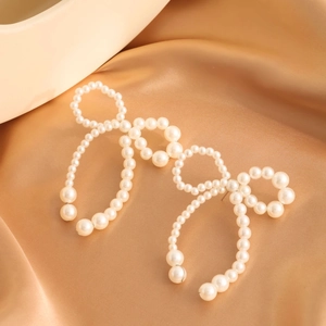 Macro shot of large pearl bow earrings on elegant gold silk fabric background