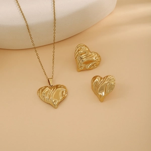 Detailed view of gold heart necklace and studs with artistic crumpled metal texture