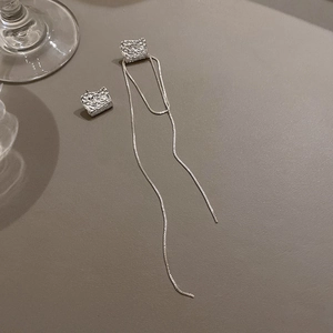 Détail de boucles d'oreilles asymétriques en argent avec textures irrégulières et longs glands