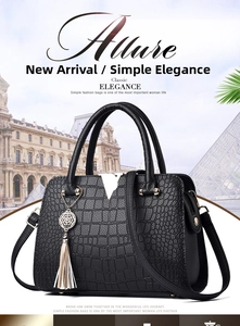 Detail of black faux crocodile handbag featuring a silver V-shaped buckle and tassel charm