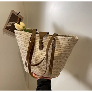 Detail of woven straw tote bag featuring brown leather straps and buckle closure