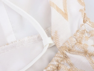 Macro shot of white woven fabric with beige geometric embroidery and thin strap detail