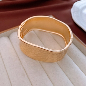 Macro view of textured wide golden bangle featuring unique hammered metal finish and hinge