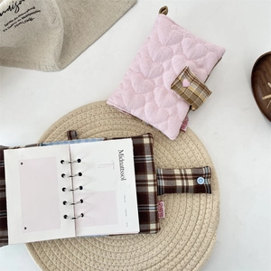Close-up of pink heart quilted and brown plaid fabric binder journals on a linen surface