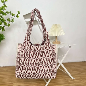 Detail of burgundy and beige wave knit tote bag hanging on a white chair in a cozy setting