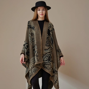 Detail of tan knit shawl with black paisley patterns shown on a model with a black wide-brim hat