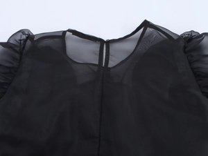 Détail de la blouse noire en organza avec épaules à volants et encolure ronde boutonnée