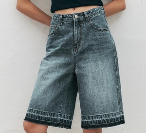 Detail of high-waist vintage blue denim shorts showing frayed hems and metallic buttons