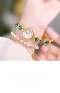 Close-up of elegant gold watch with green inlay and matching pearl bracelet for women