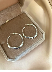 Close-up of irregular silver hoop earrings inside a premium beige velvet jewelry box