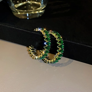 Detailed view of gold C-shaped earrings with inlaid green marquise-cut stones