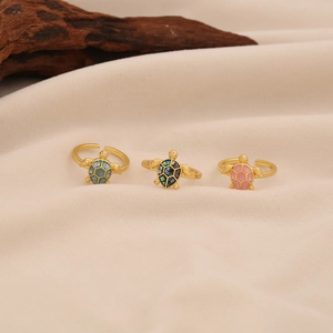 Three gold sea turtle open rings with colorful natural shell inlays on soft beige fabric