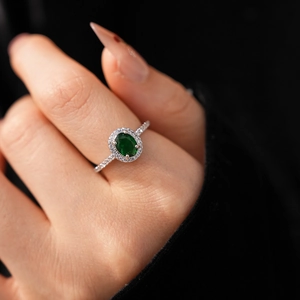Close-up of sparkling oval emerald green gemstone ring with halo diamond setting