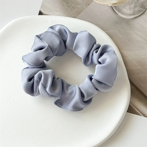 Détail macro du chouchou en satin bleu clair brillant avec plis sur plateau blanc