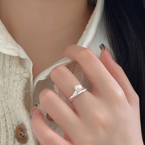 Close-up of a silver double-layered crisscross ring featuring a round white pearl on a hand