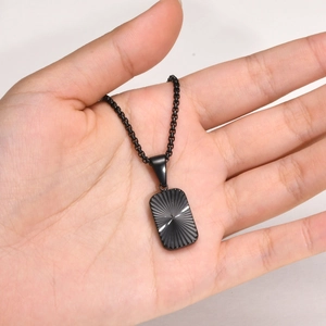 Detail of hand holding black rectangular pendant necklace with radial pattern textures