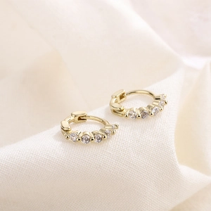 Elegant gold earrings set with five sparkling white zircons on textured linen background