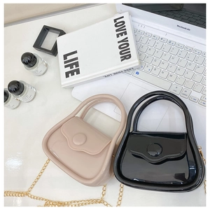 Mini glossy jelly chain bags in black and beige displayed on a desk with elegant props