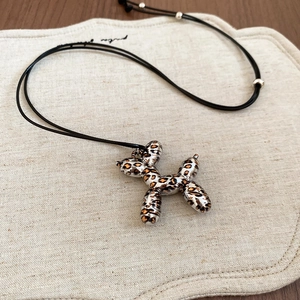 Detail of leopard print balloon dog pendant with black cord on beige linen surface