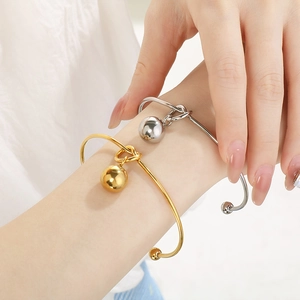 Minimalist 18K gold knot cuff bracelet with hollow steel bead pendant worn on wrist