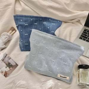 Detailed close-up of denim cosmetic bags with white bow embroidery on soft fabric