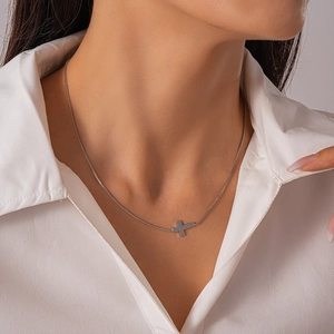 Detail view of a silver minimalist cross pendant necklace on a model with white shirt