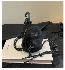 Close-up of mini black nylon backpack accessory with fashion label and woven lanyard