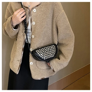 Detail of a black half-moon rivet crossbody bag with a wide woven strap on a beige coat