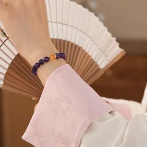 Elegant amethyst beaded bracelet with golden charm shown on wrist with a paper fan