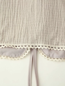 Detailed close-up of grey crinkled gauze fabric with white lace trim and lilac piping