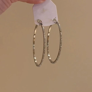 Detailed close-up of large silver hoop earrings featuring a frosted matte textured finish