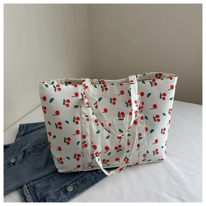 Close-up of white canvas tote bag with red cherry prints next to a denim jacket